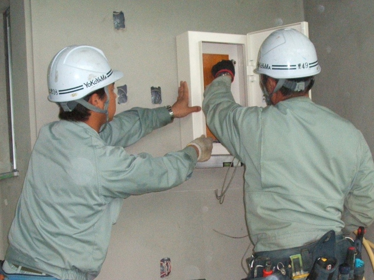 屋内の分電盤取り付け作業を行う横山電気の職人
