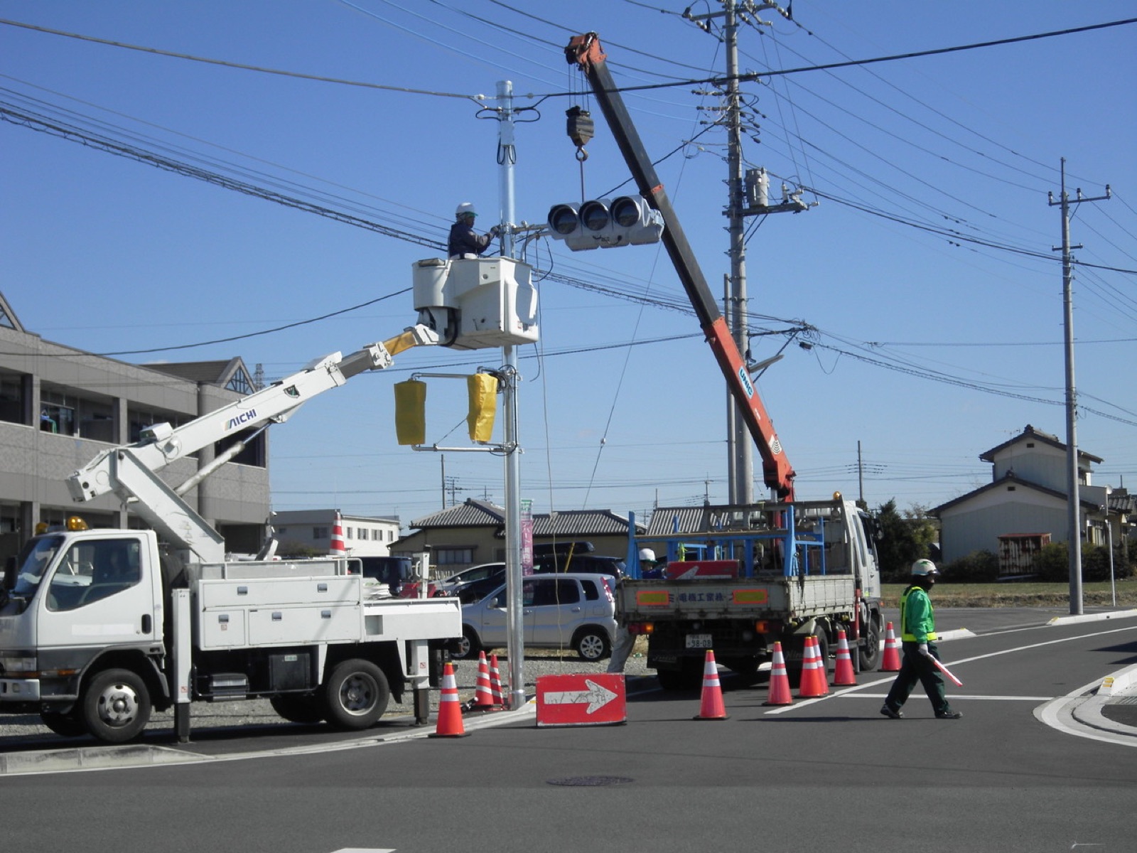 交通信号機の設置工事。高所作業車とクレーンで信号灯器を取り付けている様子